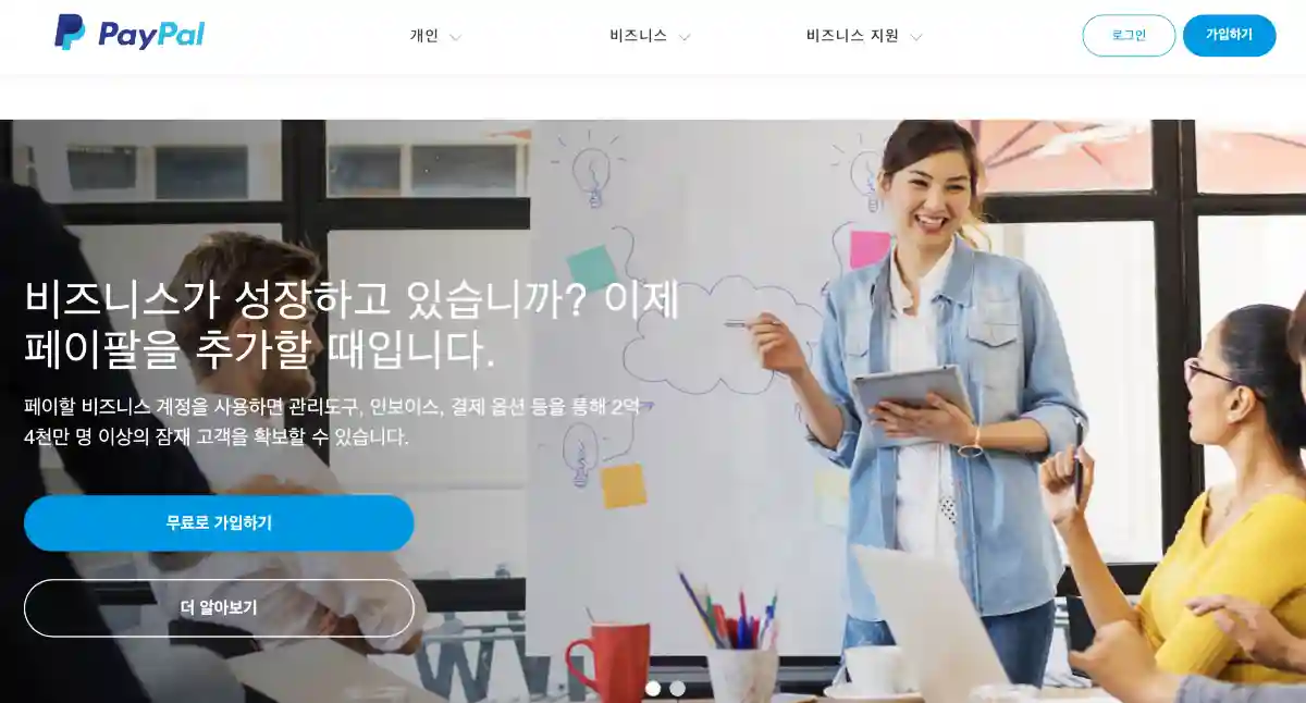 페이팔 가입 방법을 알려주기 위해 페이팔 홈페이지 이미지를 보여주고 있다. 여성 두명이 웃으면서 대화하고 있는 모습